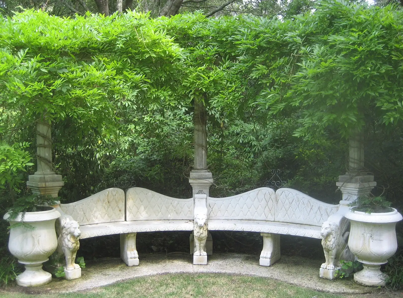 A curved stone bench with lion statues under a wisteria arbor at Airlie Gardens in Wilmington.