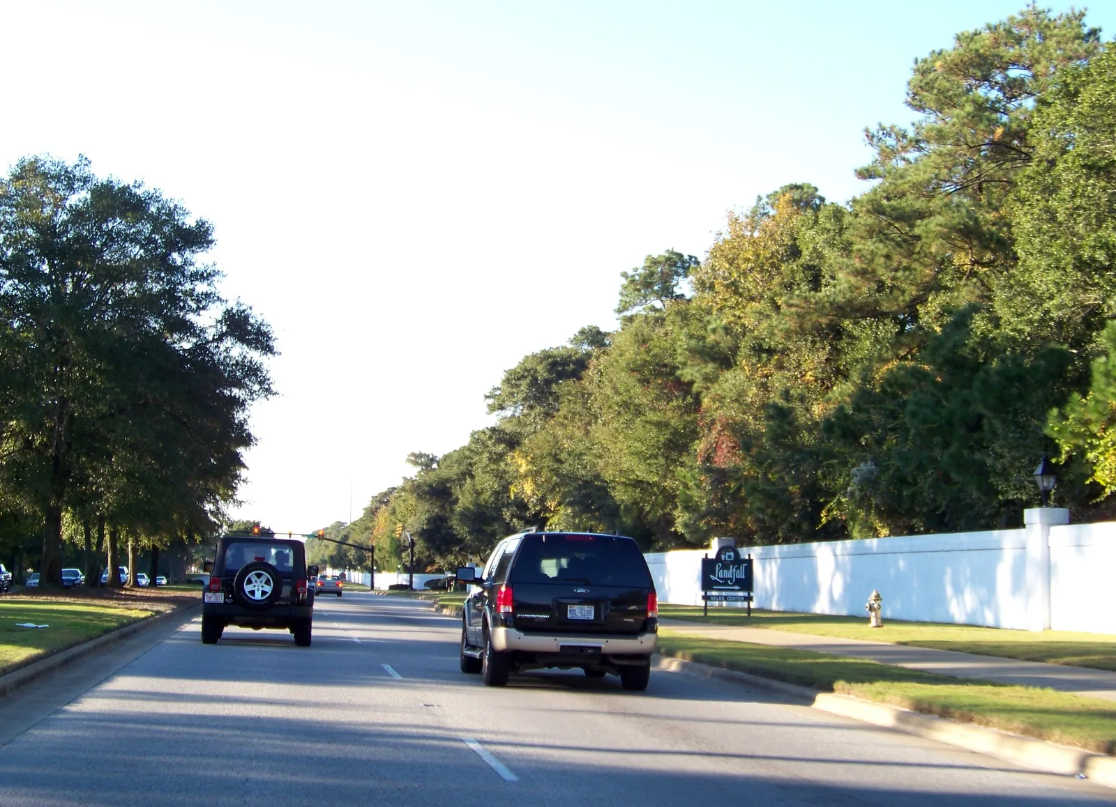 Cars on a road passing a long white wall at the edge of Landfall in Wilmington.